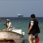 Homens armados em praia do Iêmen com navio cargueiro ao fundo