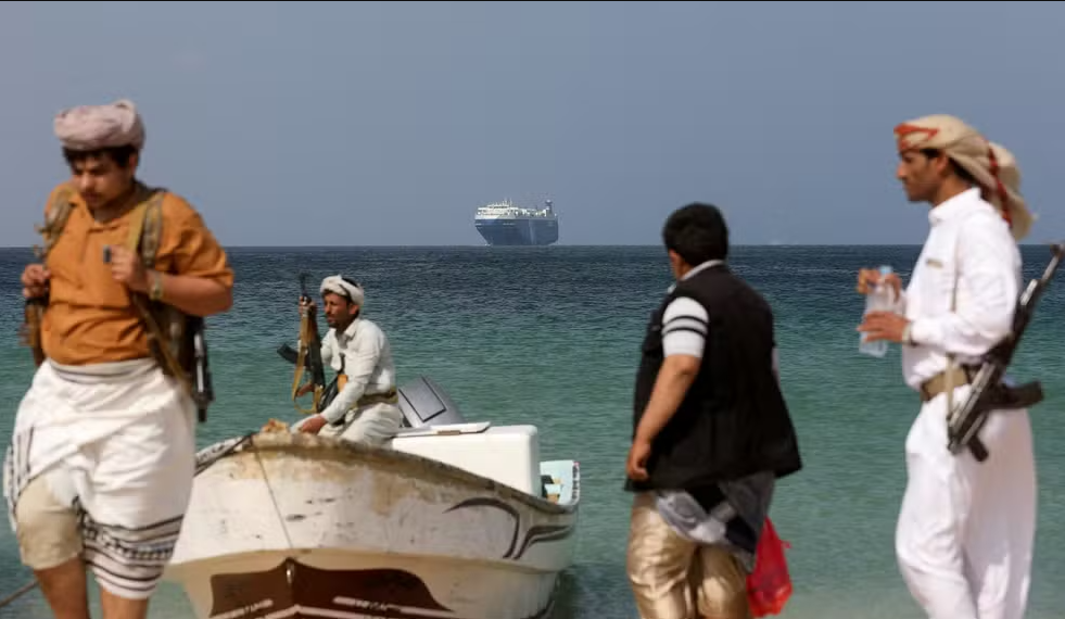 Homens armados em praia do Iêmen com navio cargueiro ao fundo